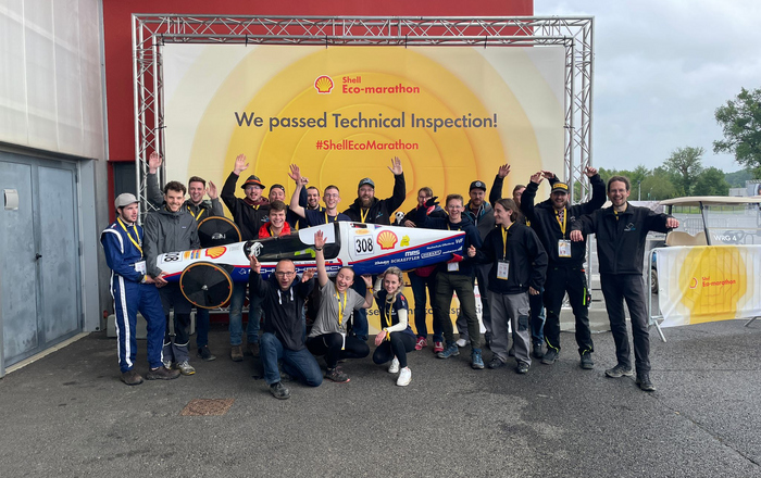 Jubelndes Team mit Schluckspecht 6 vor "We passed Technical Inspection" Banner.  