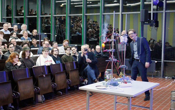 In einem Vorlesungssaal sitzende Personen verfolgen ein Experiment mit einer glühenden Gurke