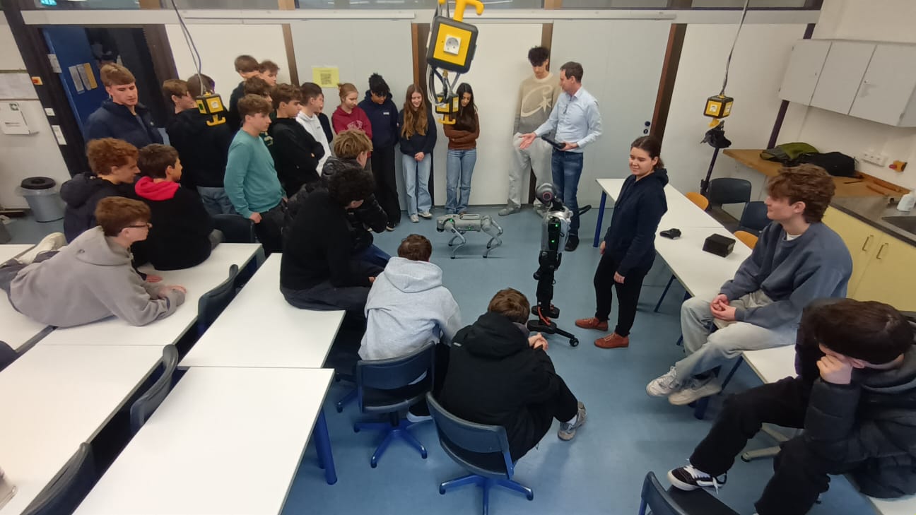 Schüler*innen stehen in einem Klassenraum um einen humanoiden Roboter und einen Roboter-Hund herum
